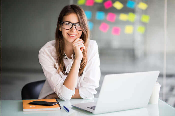 Mulher sorrindo enquanto mexe no seu notebook.