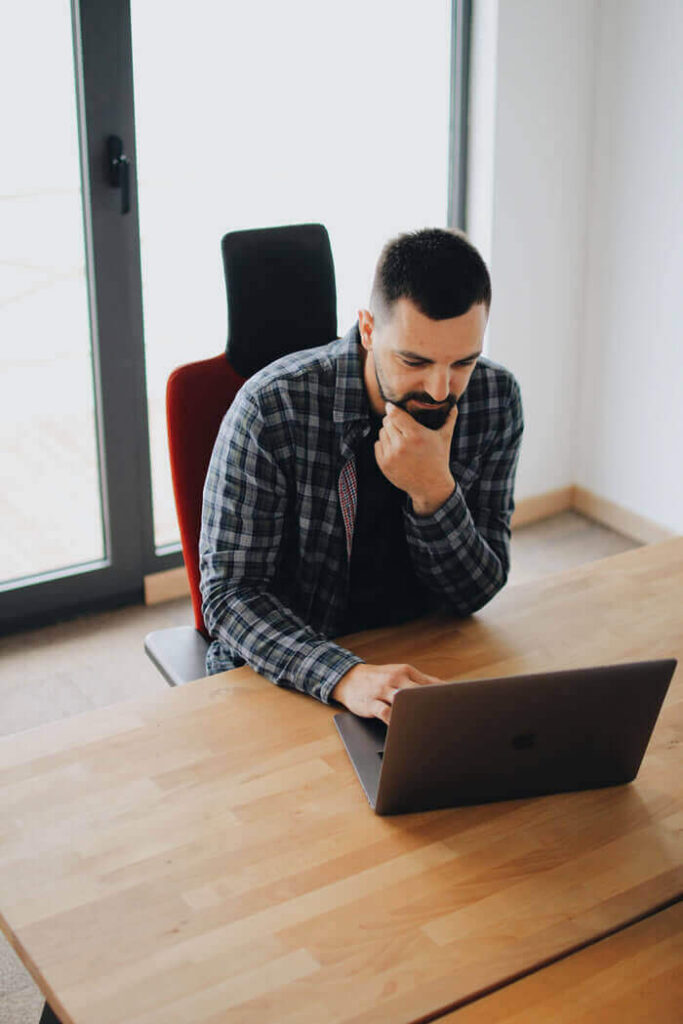 Homem mexendo no seu notebook enquanto está pensando.